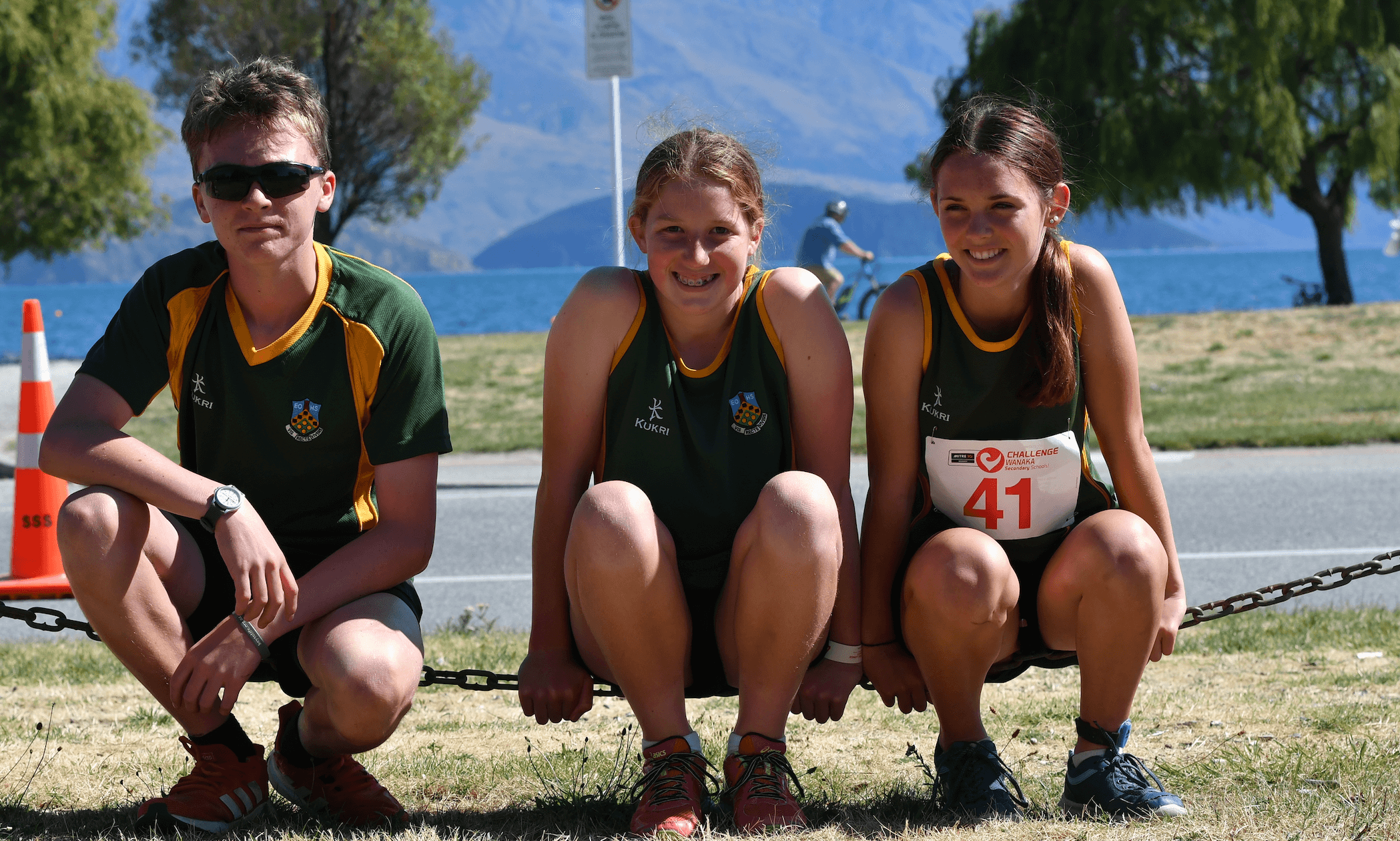 three sports students sitting on a chain with lake in background
